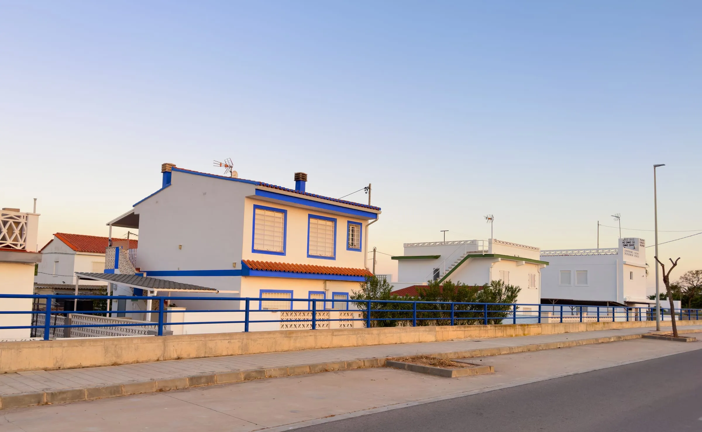 Casa blanca con carpinterías azules junto al paseo marítimo al atardecer