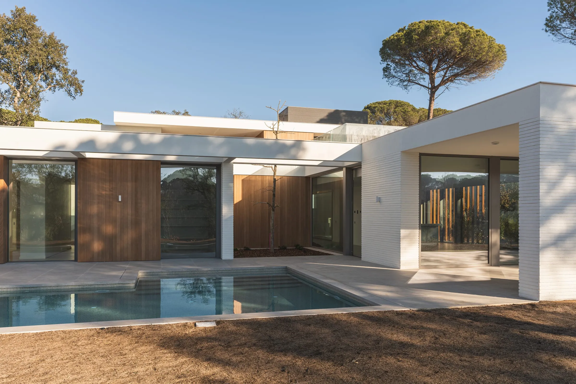 Casa moderna de una planta en blanco y madera con piscina entre pinos