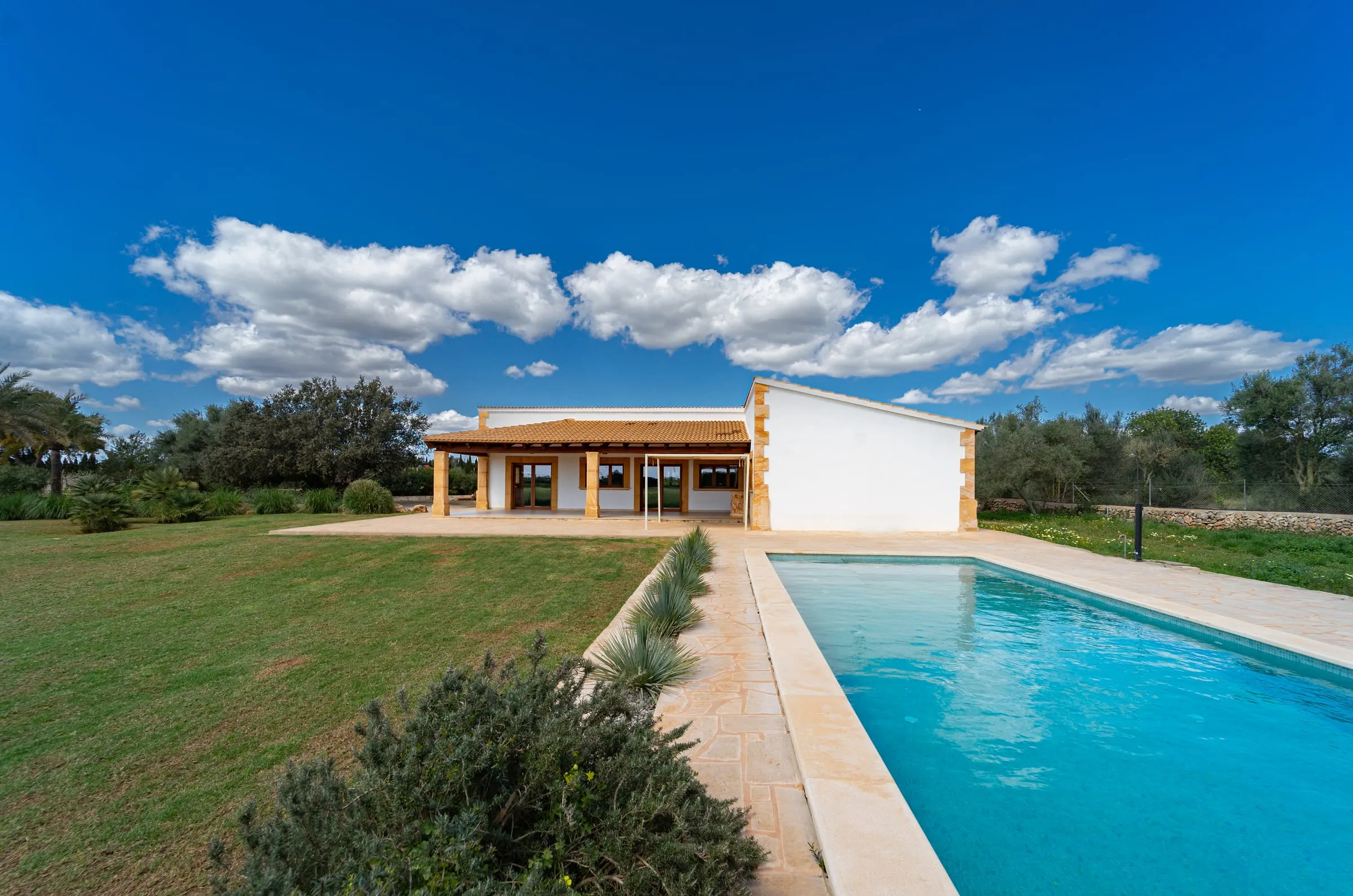 Casa de campo de una planta con porche y piscina en una parcela de césped