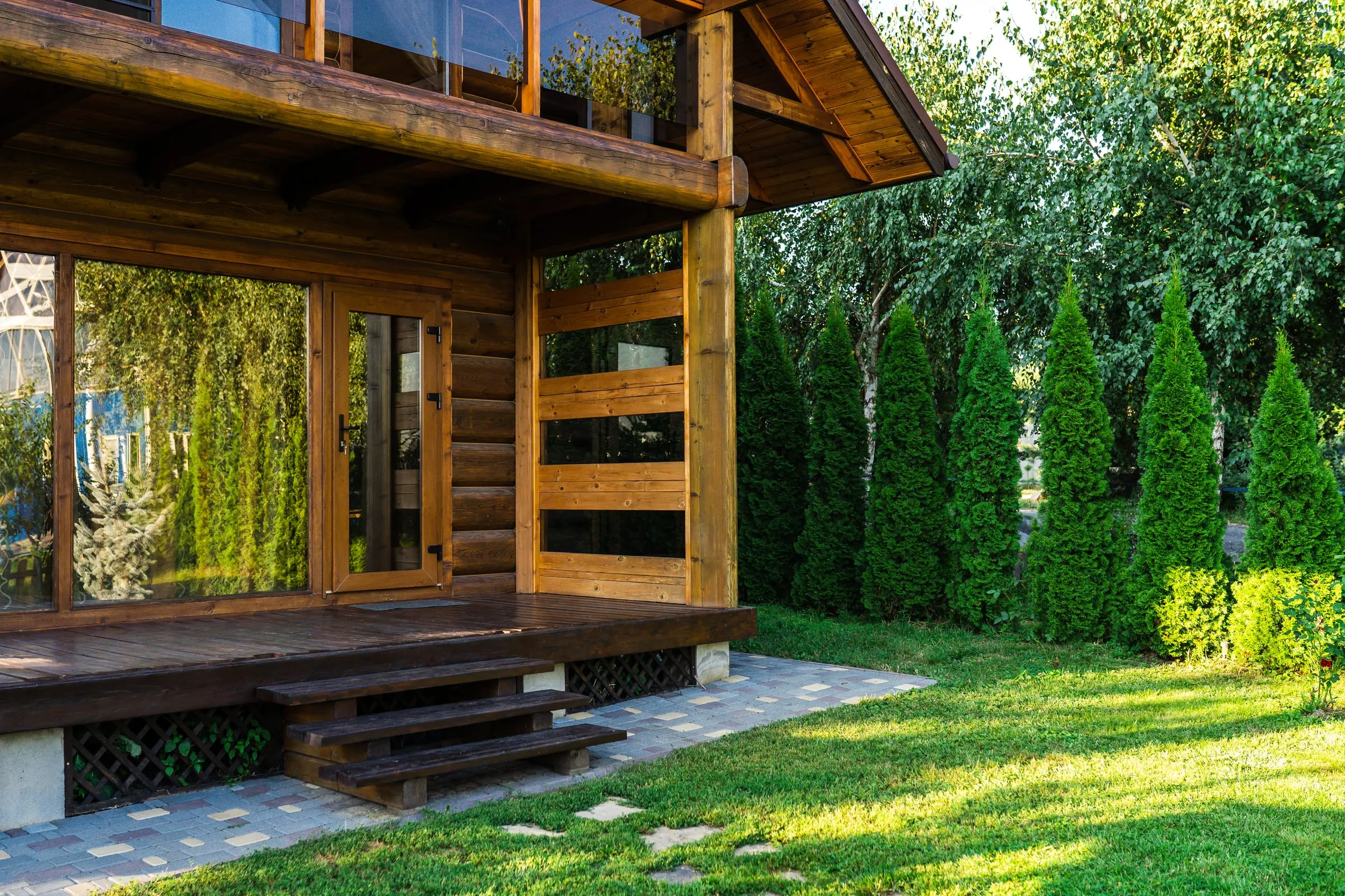 Porche de una casa de madera con jardín y seto de tuyas