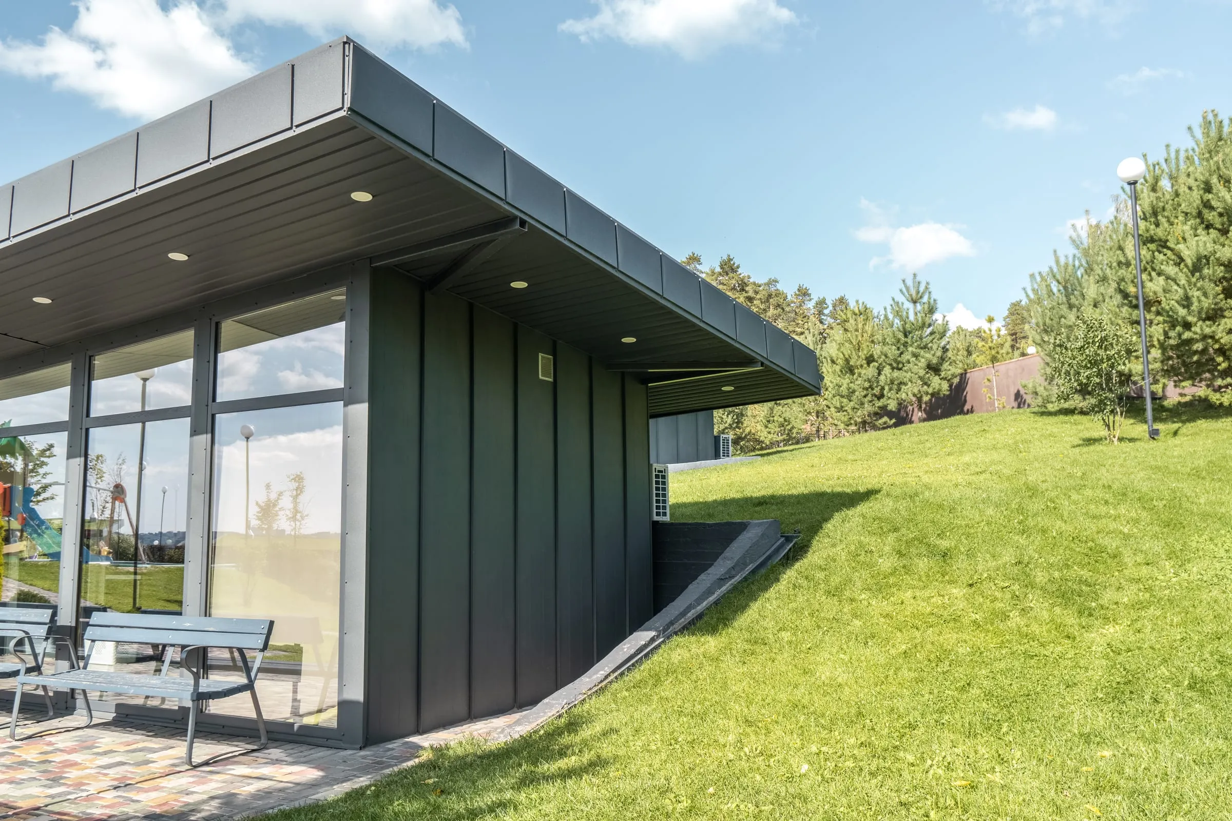 Casa moderna de una planta con fachada de chapa, grandes ventanales y jardín de césped